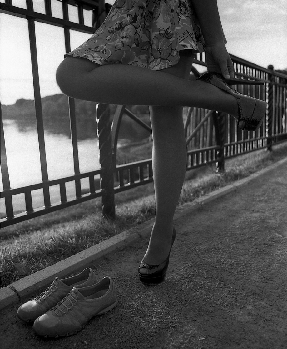 A slender girl in a short skirt changes her high-heeled shoes to sports shoes.